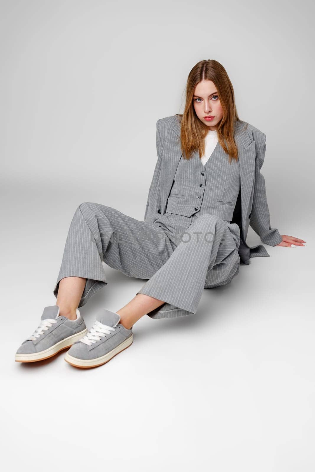 Young Woman in a Gray Suit Sitting on the Floor in Studio by Fabrikasimf