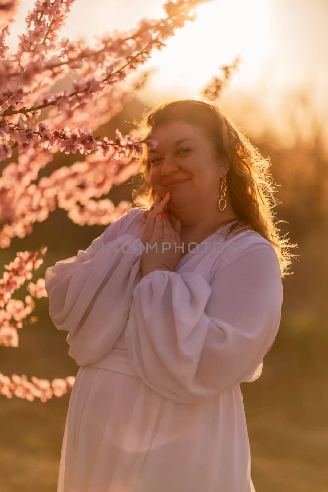 Woman blooming peach orchard. Against the backdrop of a picturesque peach orchard, a woman in a long white dress enjoys a peaceful walk in the park, surrounded by the beauty of nature