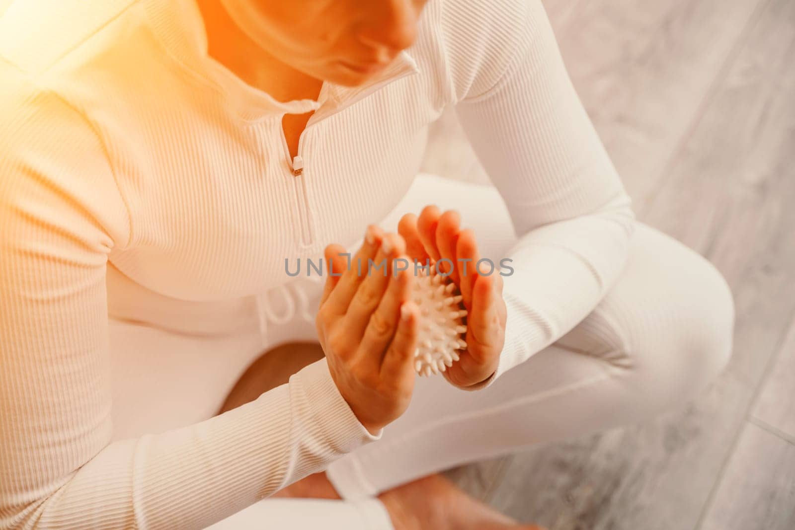 Athletic slim caucasian woman doing thigh self-massage with a massage ball indoors. Self-isolating massage by Matiunina
