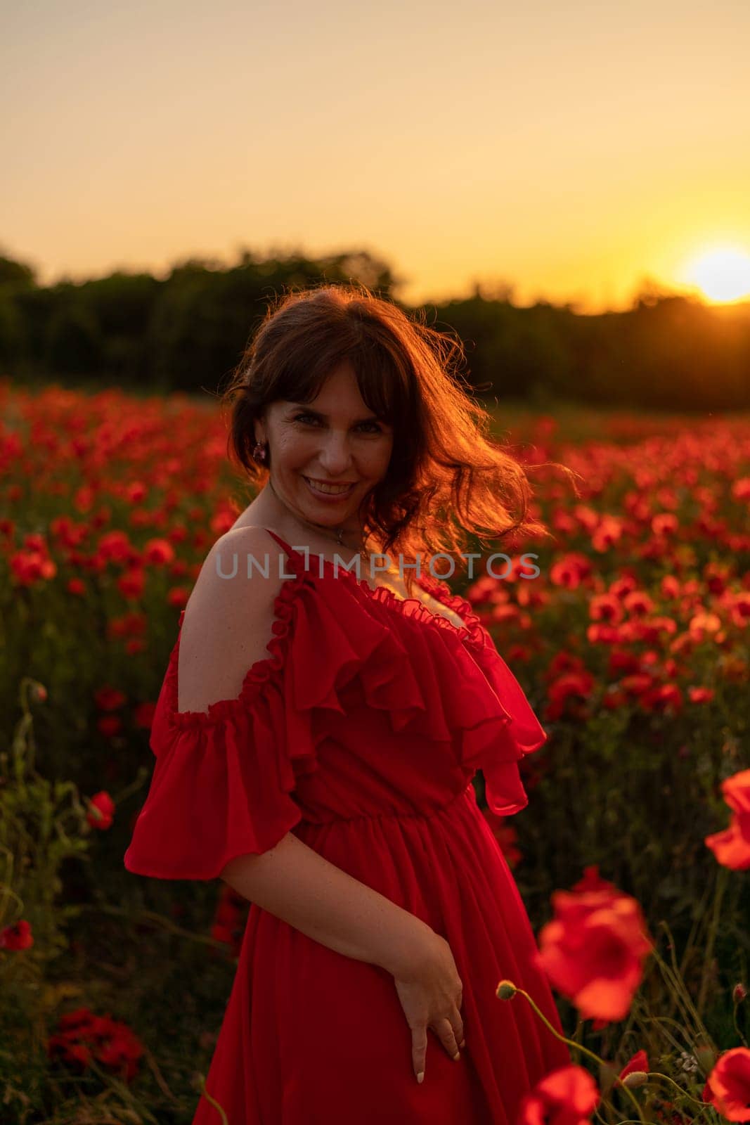Woman poppy field red dress sunset. Happy woman in a long red dress in a beautiful large poppy field. Blond stands with her back posing on a large field of red poppies.