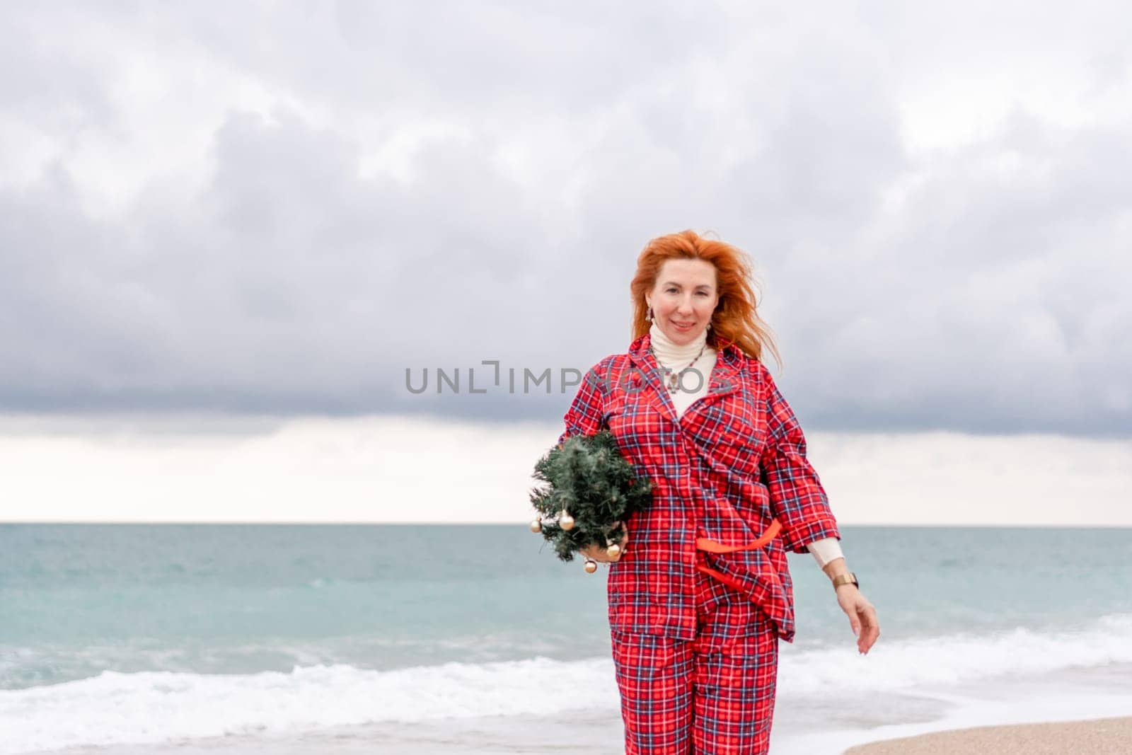 Sea Lady in plaid shirt with a christmas tree in her hands enjoys beach. Coastal area. Christmas, New Year holidays concep by Matiunina