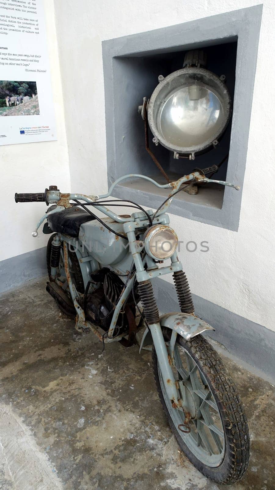 Asinara, Italy. August 11, 2021. Ancient motorcycle and a large headlight at the entrance to the prison museum. by Jamaladeen