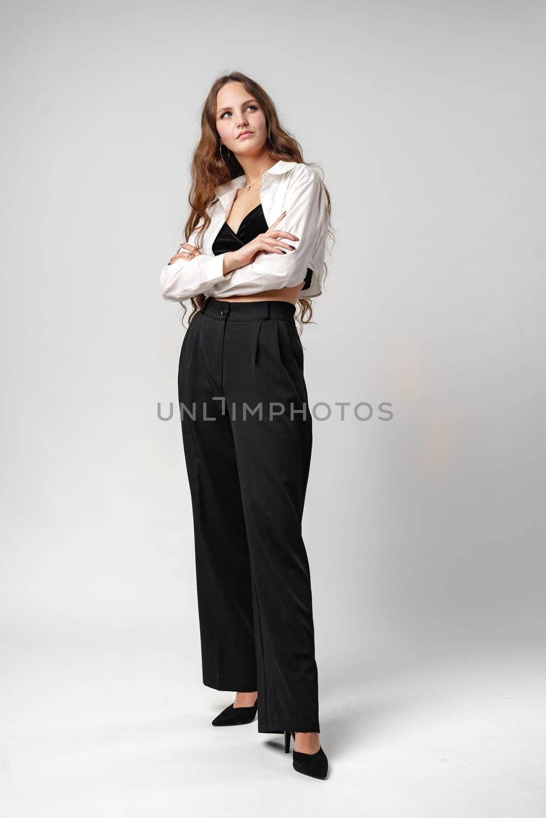 A woman is standing wearing a white shirt and black pants. She appears to be posing for a photograph or just enjoying a moment. The neutral colors of her outfit contrast nicely and create a simple yet classic look.