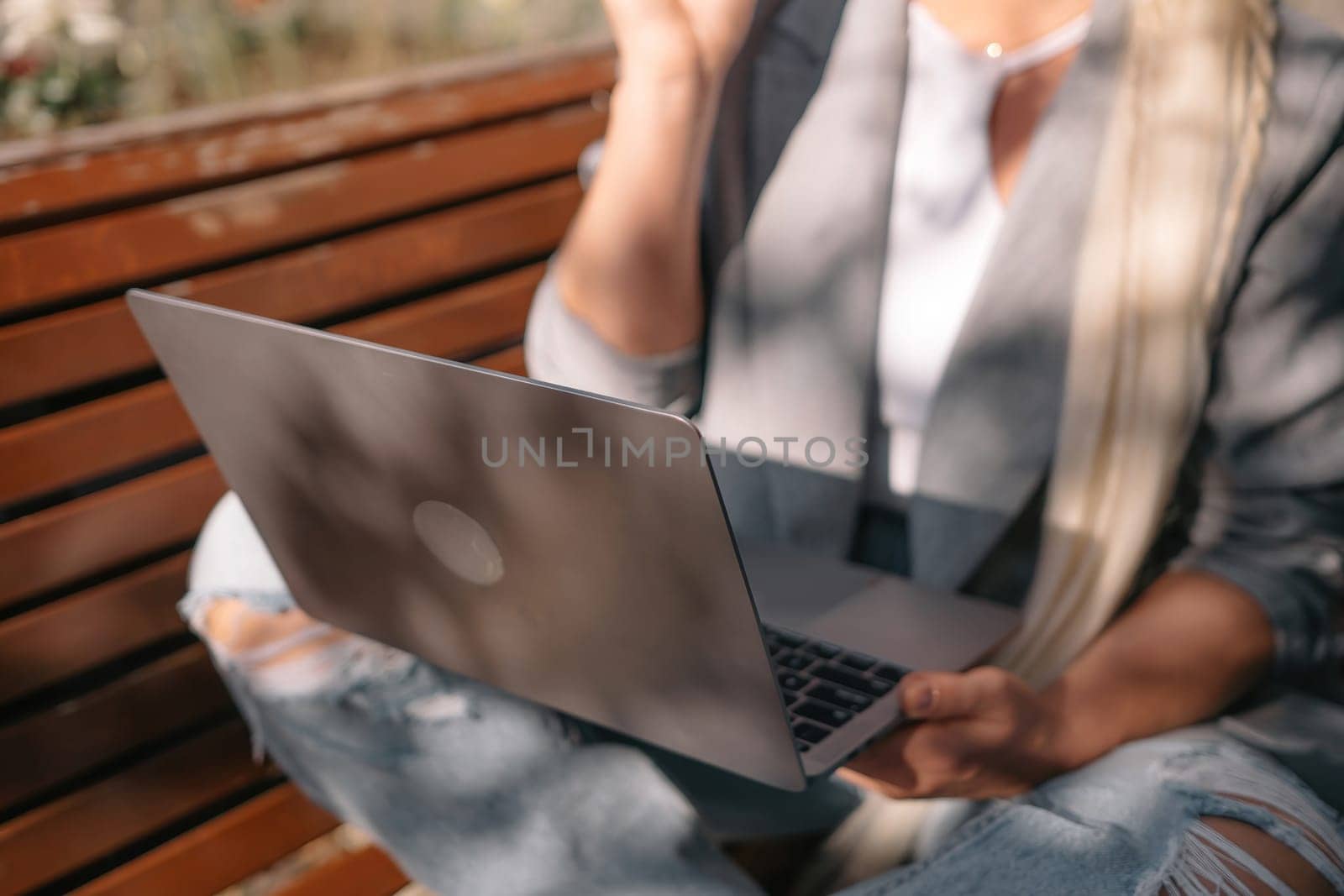 A woman is sitting on a bench with a laptop in front of her. She is wearing a gray jacket and a white shirt