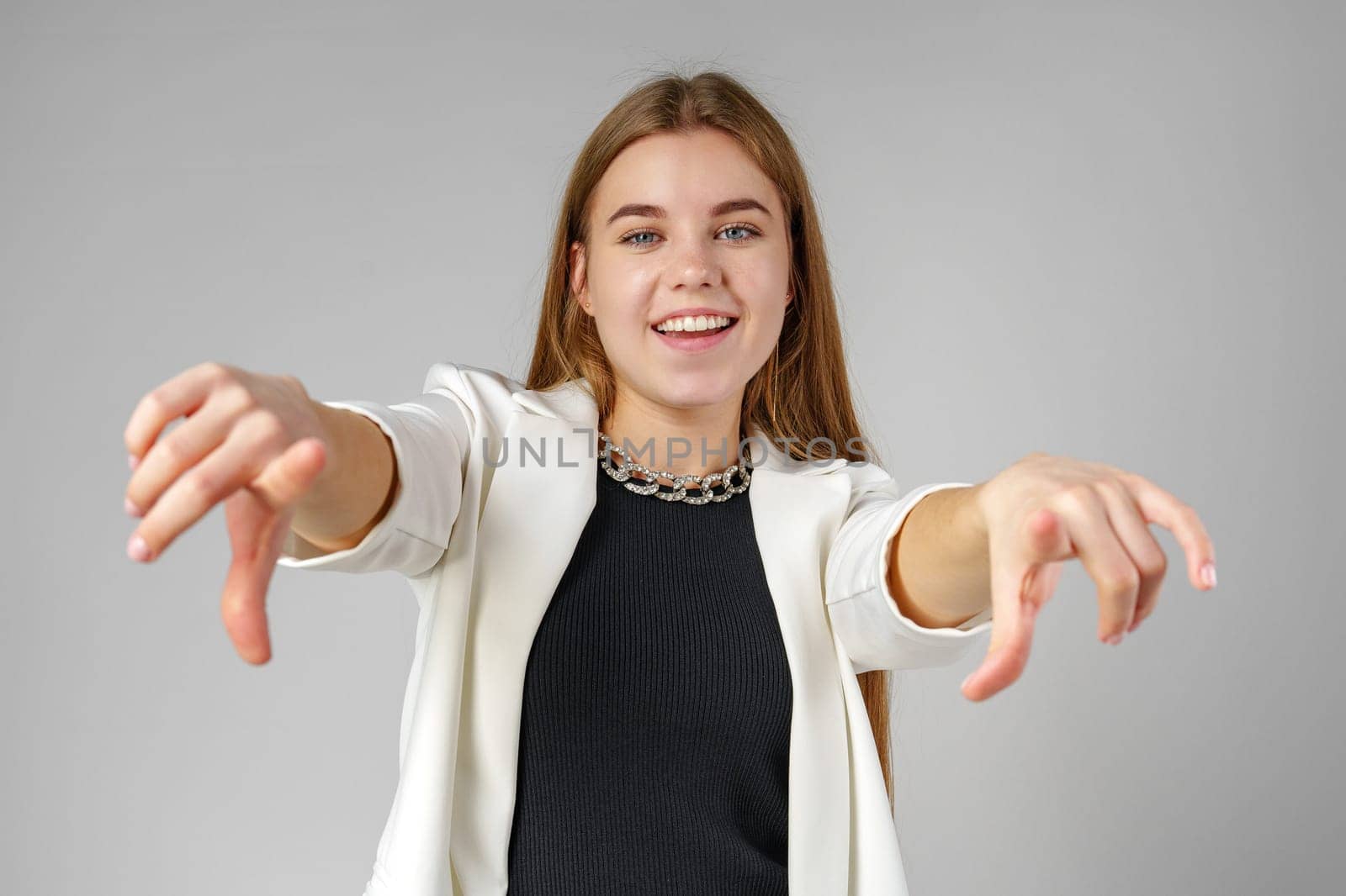 Young Woman in White Blazer Pointing at You Against a Grey Background by Fabrikasimf