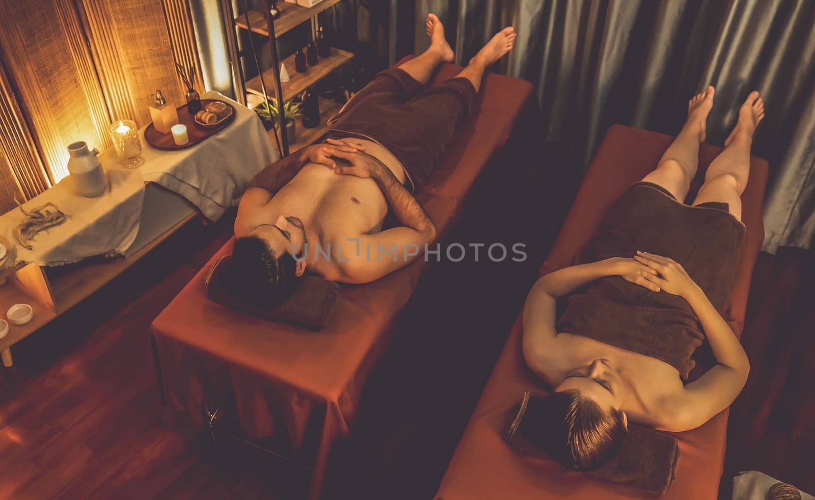 Caucasian couple customer enjoying relaxing anti-stress spa massage and pampering with beauty skin recreation leisure in warm candle lighting ambient salon spa at luxury resort or hotel. Quiescent