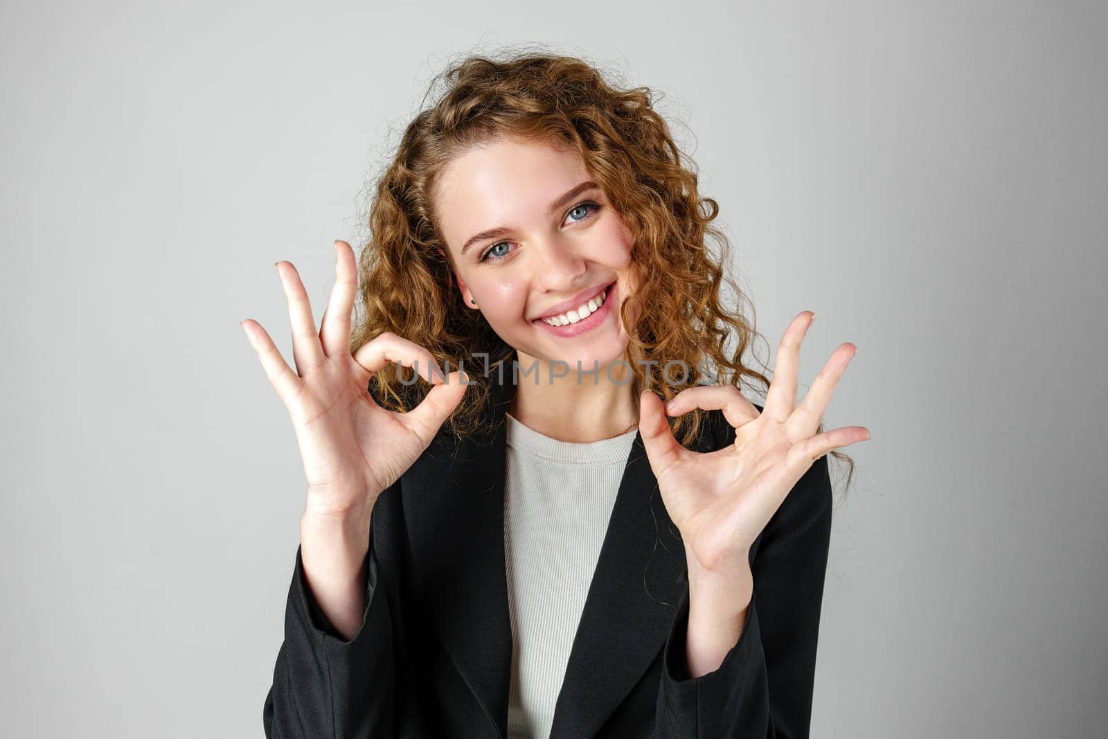Young Woman Giving Ok Sign on gray background by Fabrikasimf