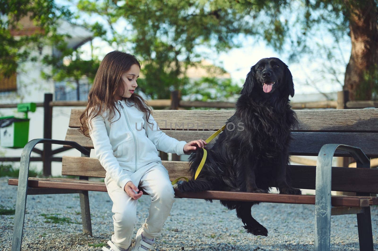 Full length portrait of a cute child nd her dog on the city bench in the nature outdoors. Cute child walking her dog on leash. People and domestic animals. Pets concept