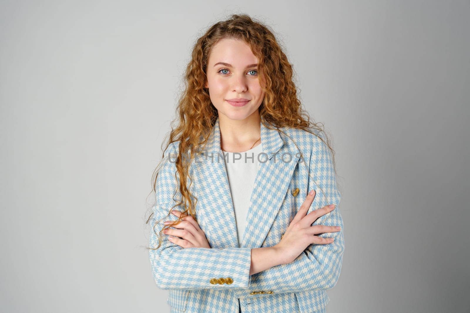 Young woman with curly hair in blue jacket posing on gray background by Fabrikasimf