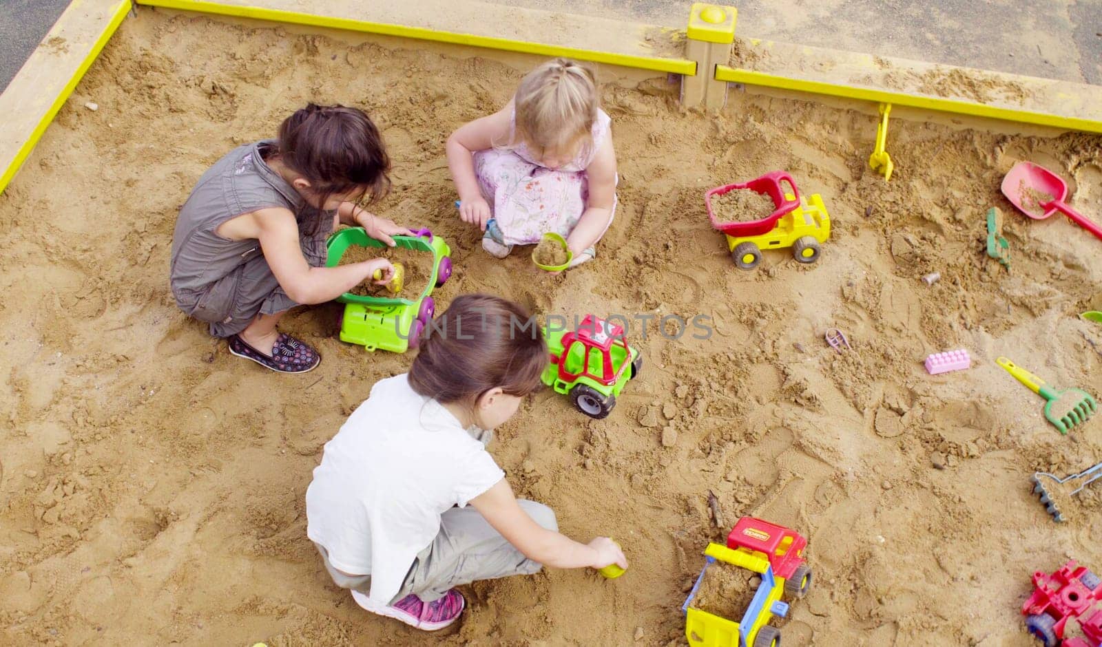 Top view. Three girls sitting in a sandbox and playing sand