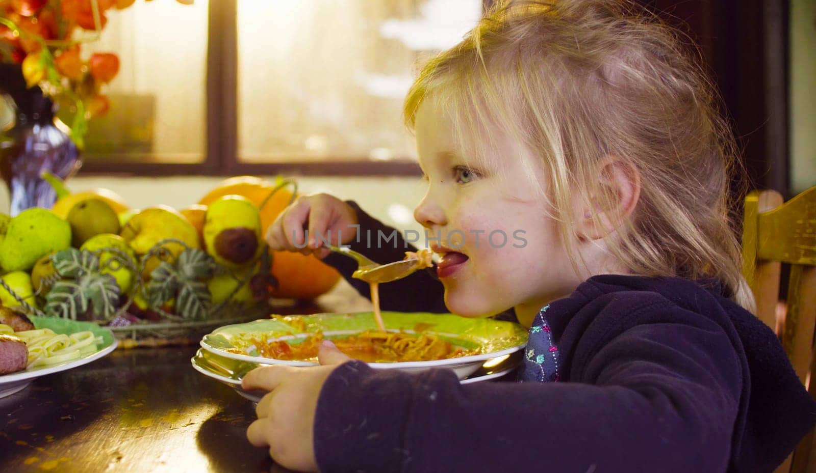 Close up portrait of little girl sitting at the table and eating soup