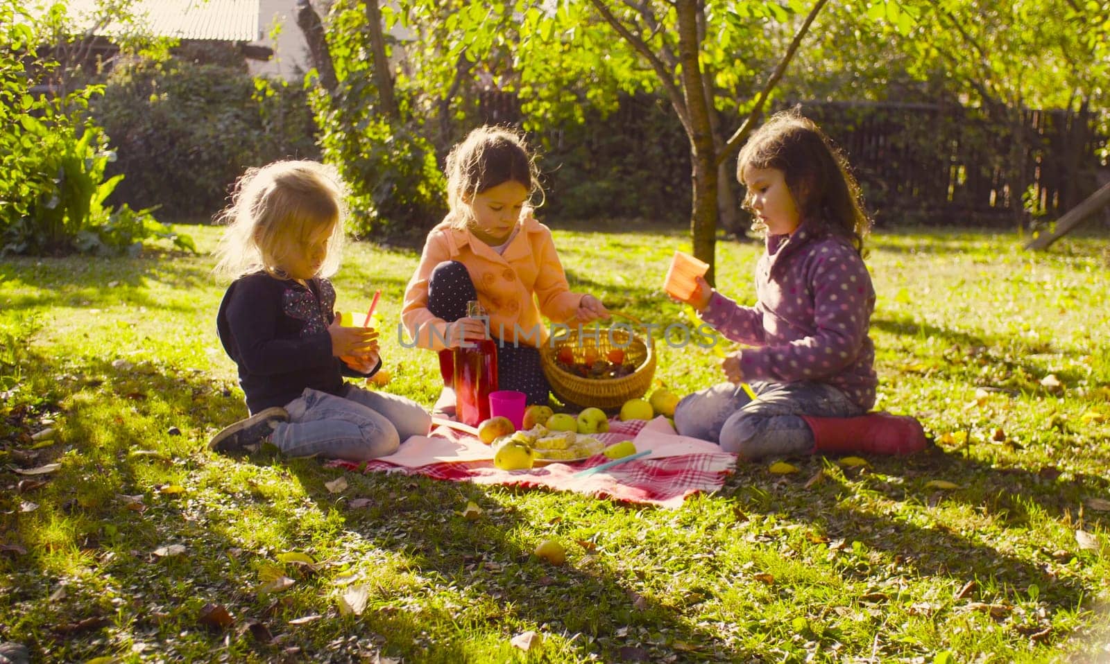 Autumn. Picnic in the garden. Children sitting on grass and drinking compote