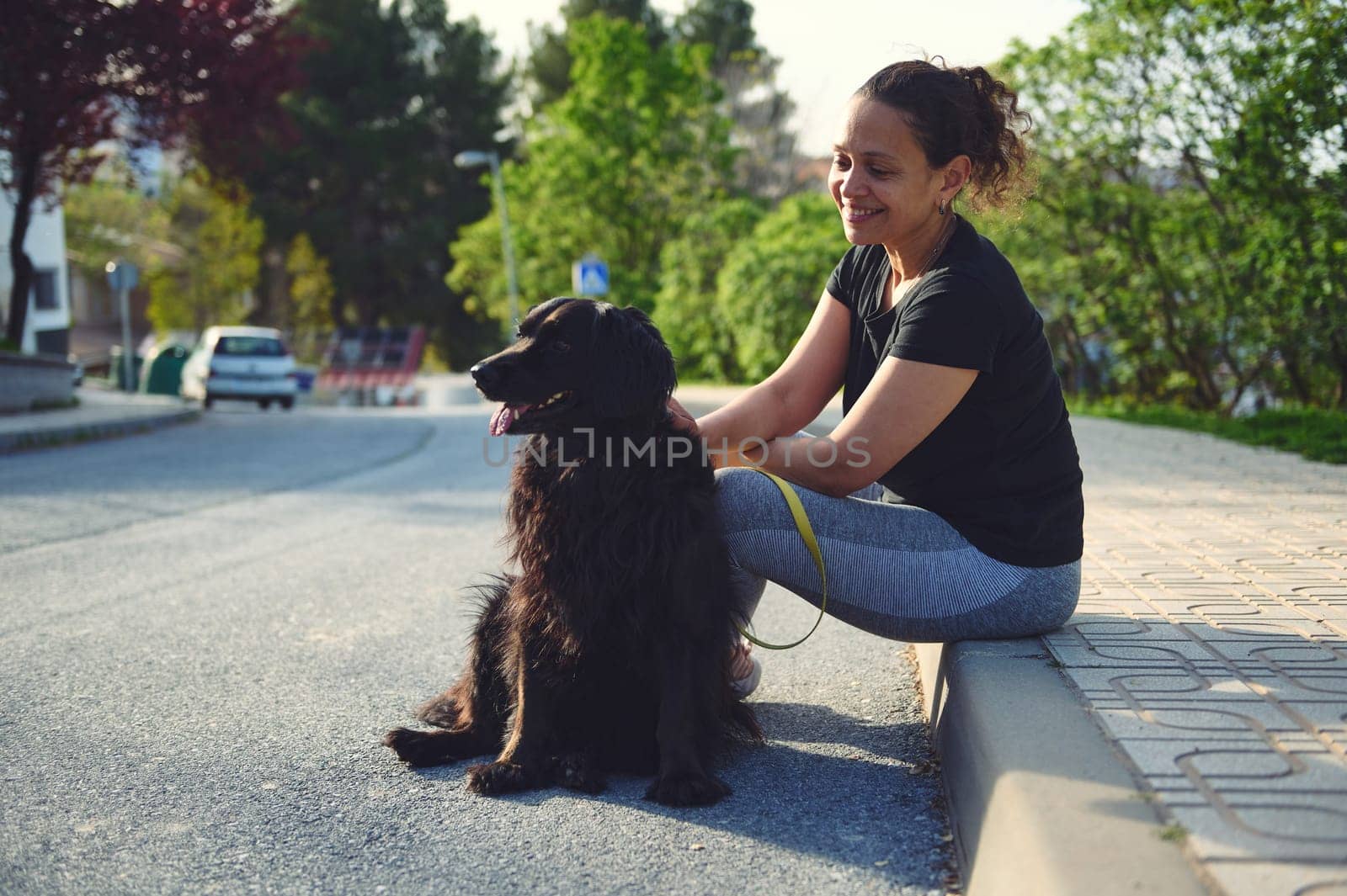 Happy young woman enjoying the outdoors with her pet dog. Pretty female walking her black cocker spaniel on leash by artgf