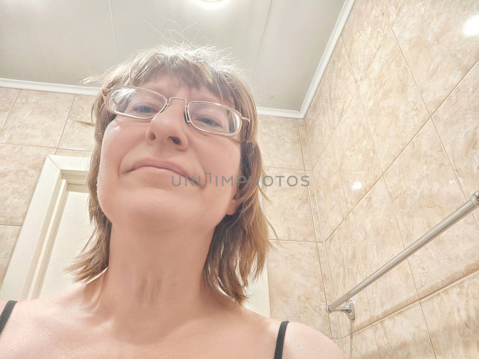 A shaggy, funny middle-aged woman in glasses takes selfie on in front of the mirror in the morning. A blogger girl with disheveled hair takes pictures of herself for a blog