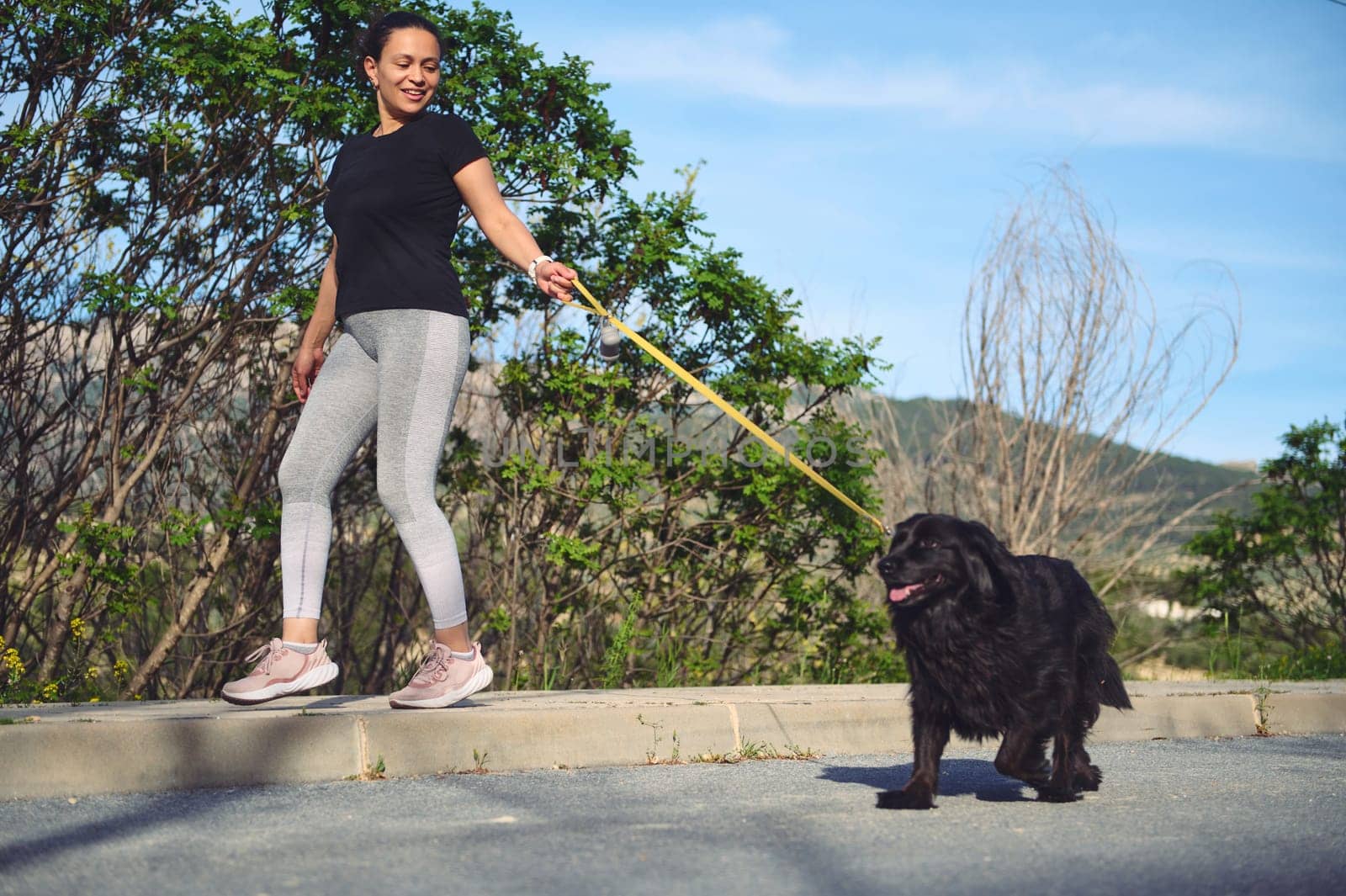 Happy female athlete, woman runner walking her dog on leash with performing morning jog on the mountains outdoors. People, nature, pets and healthy active lifestyle concept