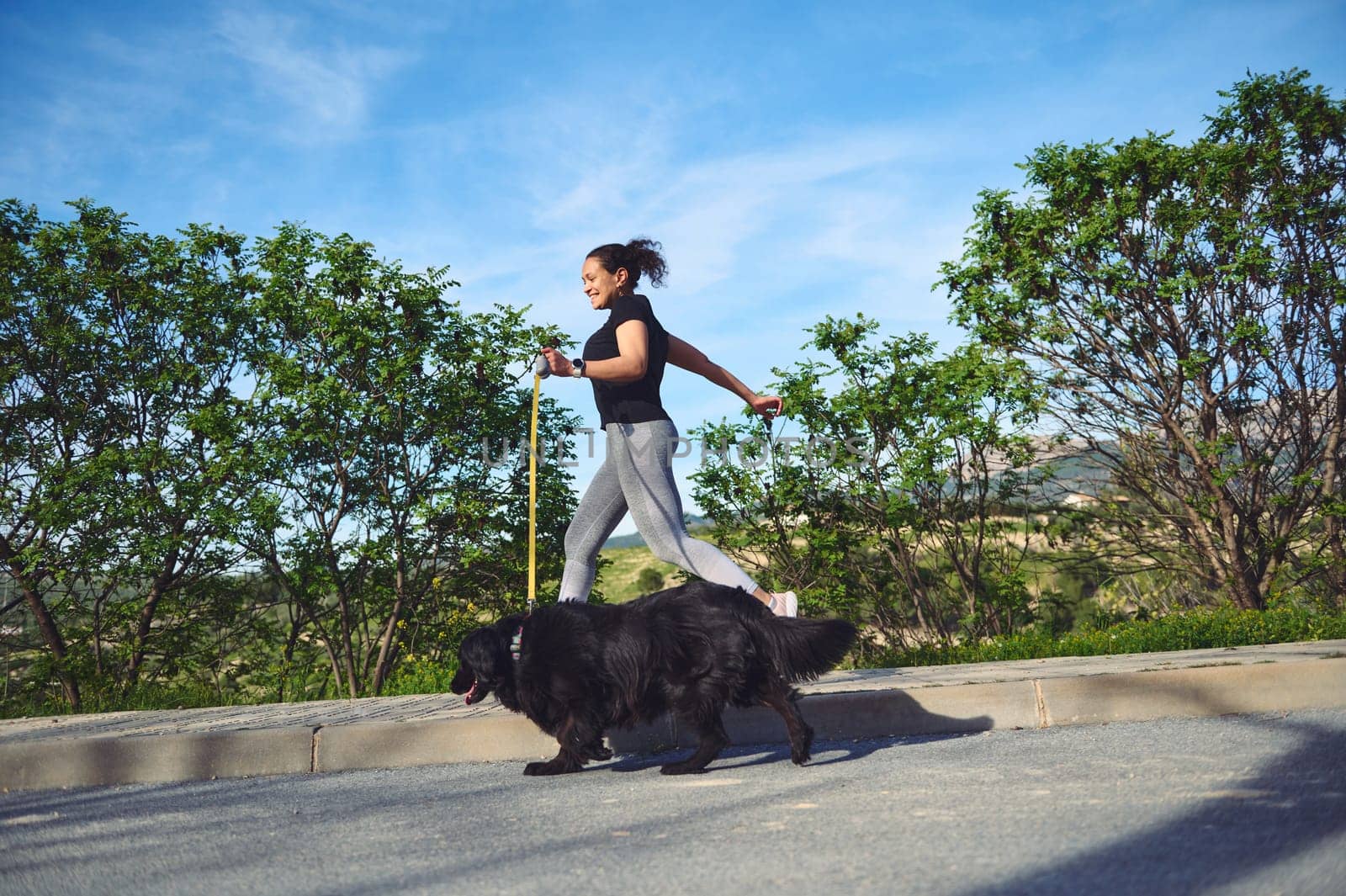Full length portrait of a happy sporty woman in motion, enjoying her morning run with her cocker spaniel dog being walked on leash on the nature. People. Playing pets. Healthy active lifestyle concept