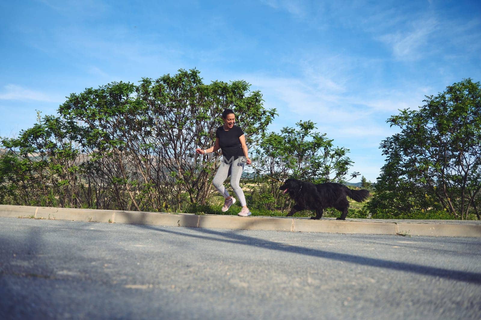 Full length authentic portrait of a cheerful woman running with her pet on leash, as perfect way to walk a dog and to exercise outdoors. Playing pets concept by artgf