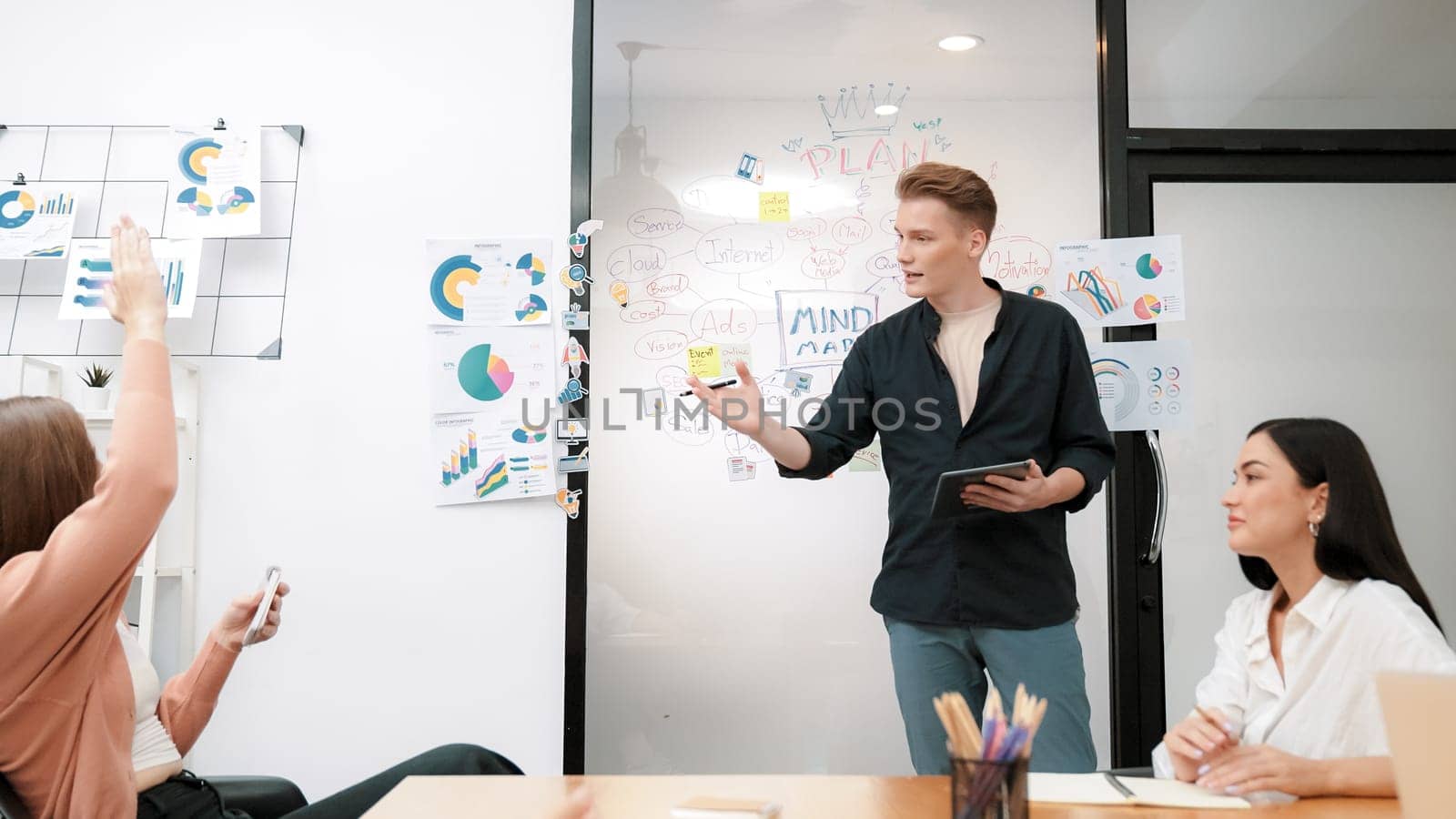 Professional male leader presents start up project by using mind map, colorful sticky notes and business statistic graph with confident while investor raising hand and asking question. Immaculate.