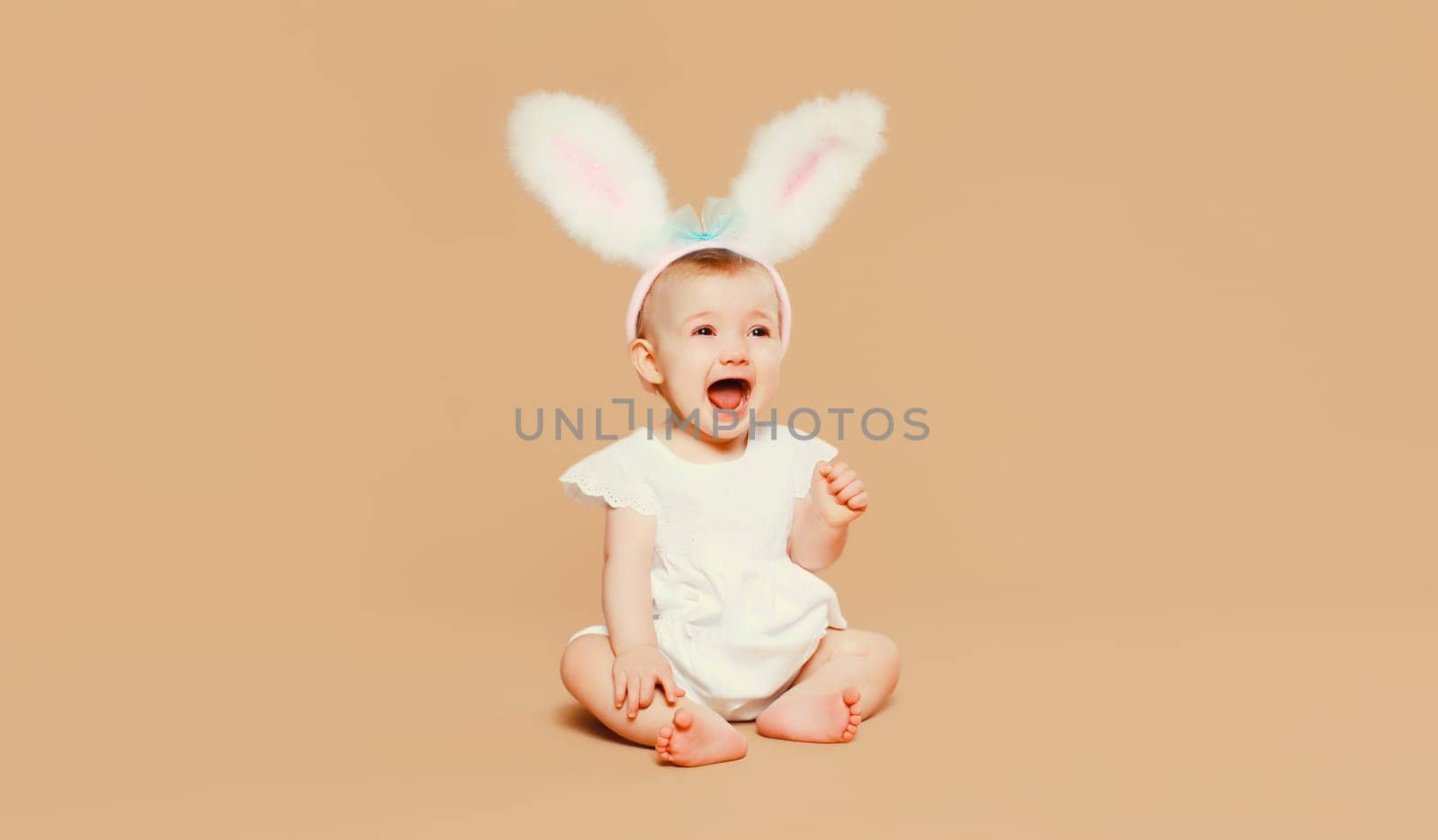 Portrait cute baby with easter rabbit ears sitting on brown studio background by Rohappy