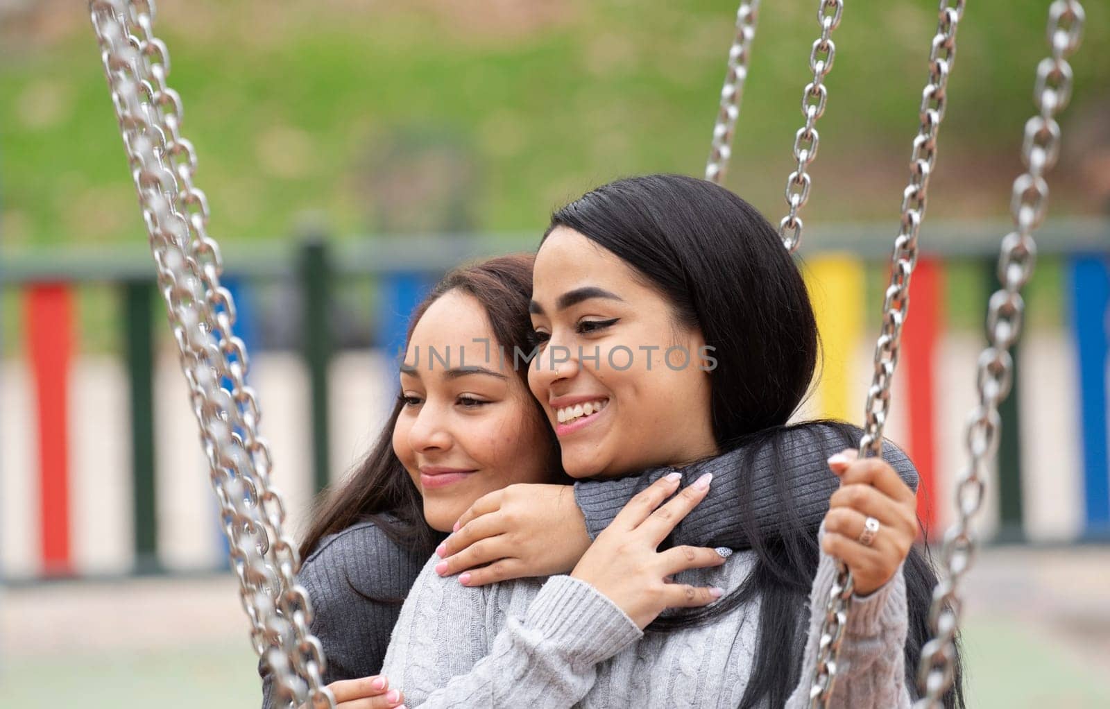 Headshot of two happy young women hugging on a swing.