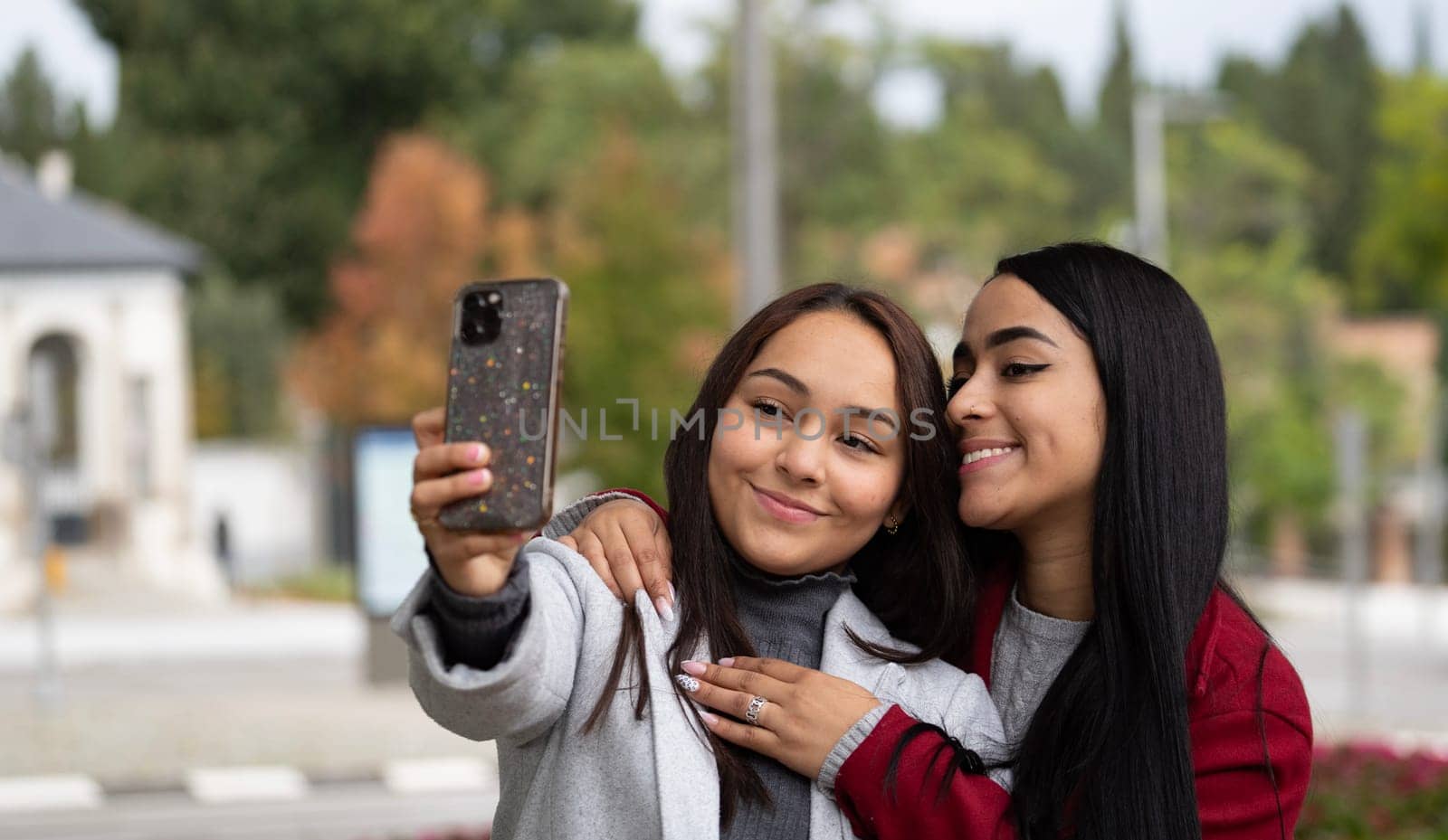 Two smiling lesbian couple latin women are taking a selfie together outdoors.