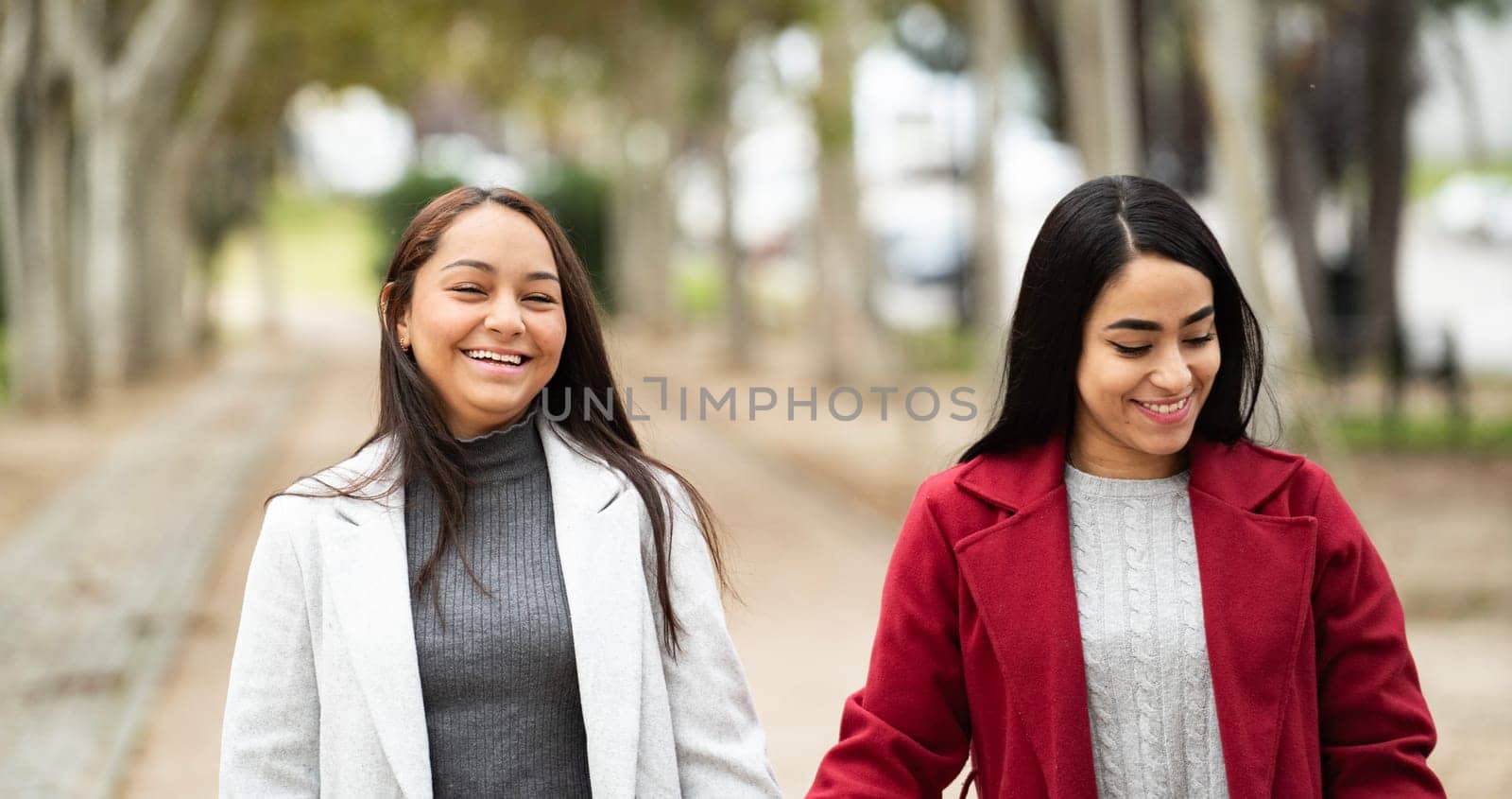 Two latin women are walking in a park smiling, laughing and enjoying their time together.