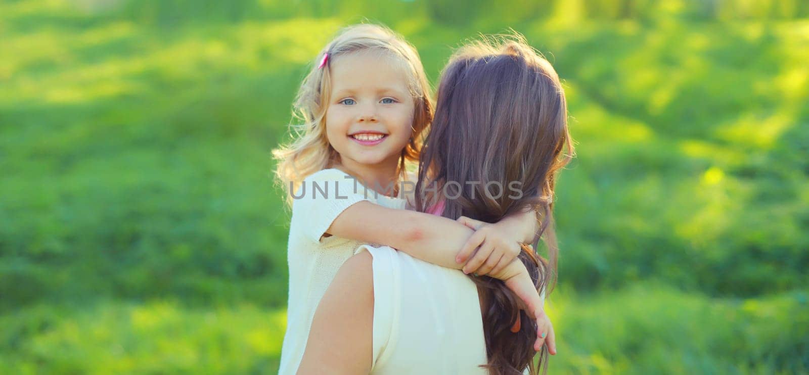 Portrait of happy cheerful smiling mother with little girl child daughter on the grass in sunny summer park