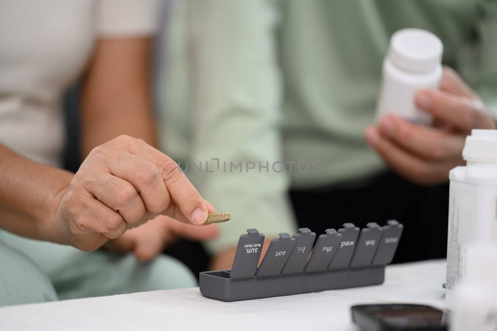 Senior woman hands taking a pill from weekly organizer. Health care, medicine and treatment concept.