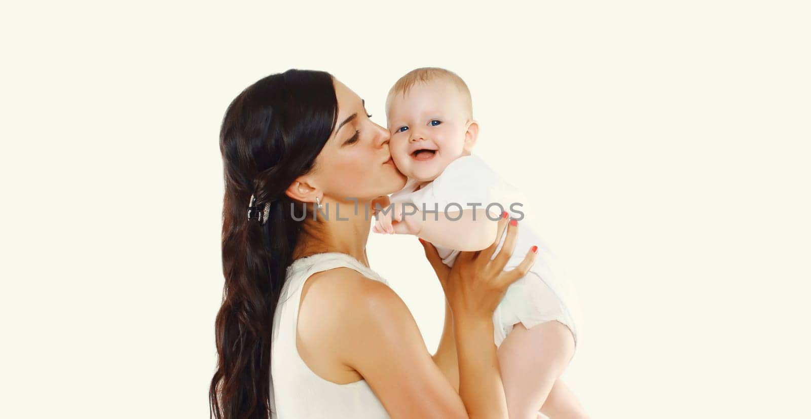 Happy young mother holding and kissing baby on white studio background