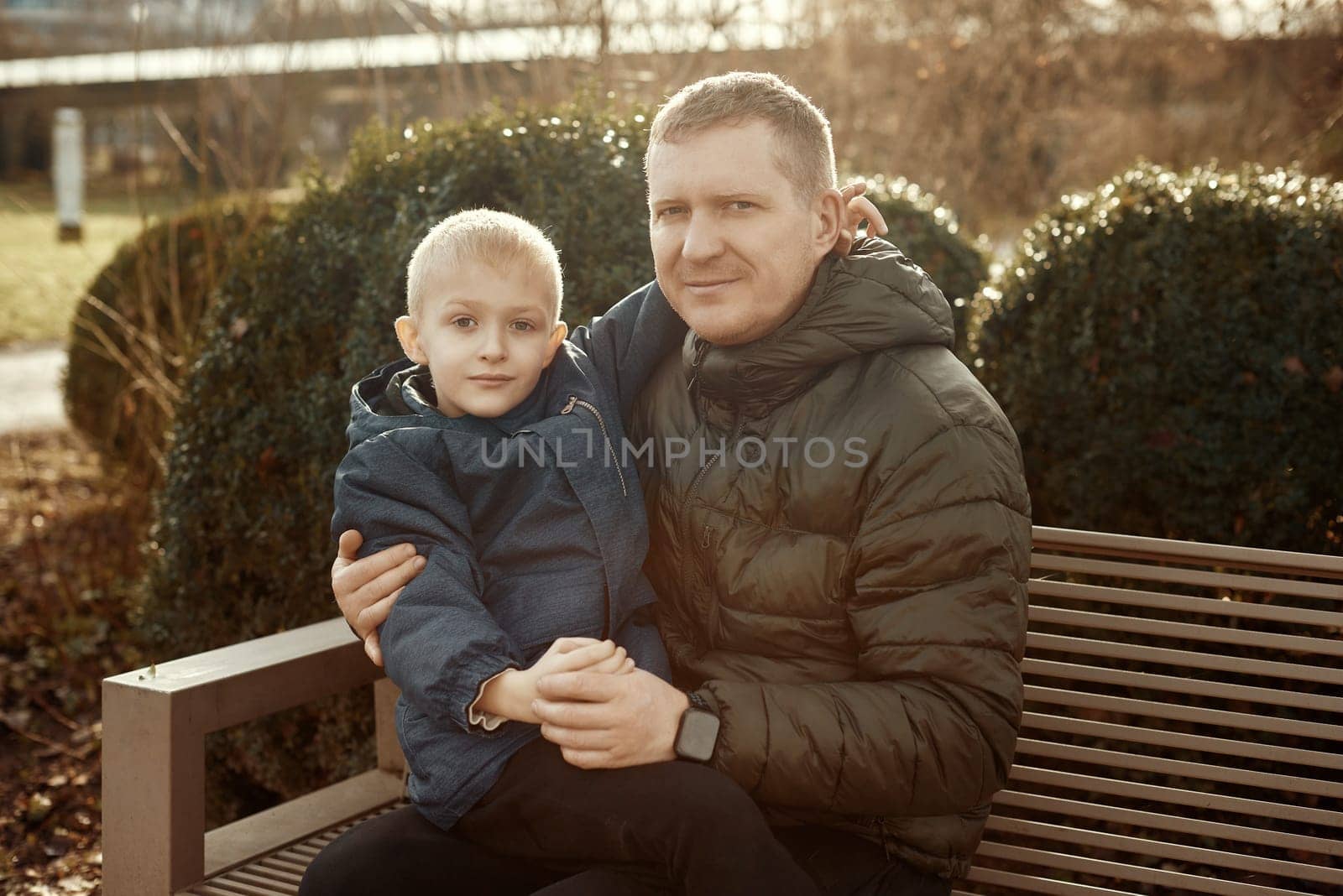 Autumnal Family Affection: Father, 40 Years Old, and Son - Beautiful 8-Year-Old Boy, Seated in the Park. Embrace the warmth of familial love in the autumnal air with this heartwarming image. A father, 40 years old, and his son - a beautiful 8-year-old boy, seated in the park. The essence of autumn adds a touch of seasonal charm to this delightful moment of family affection.