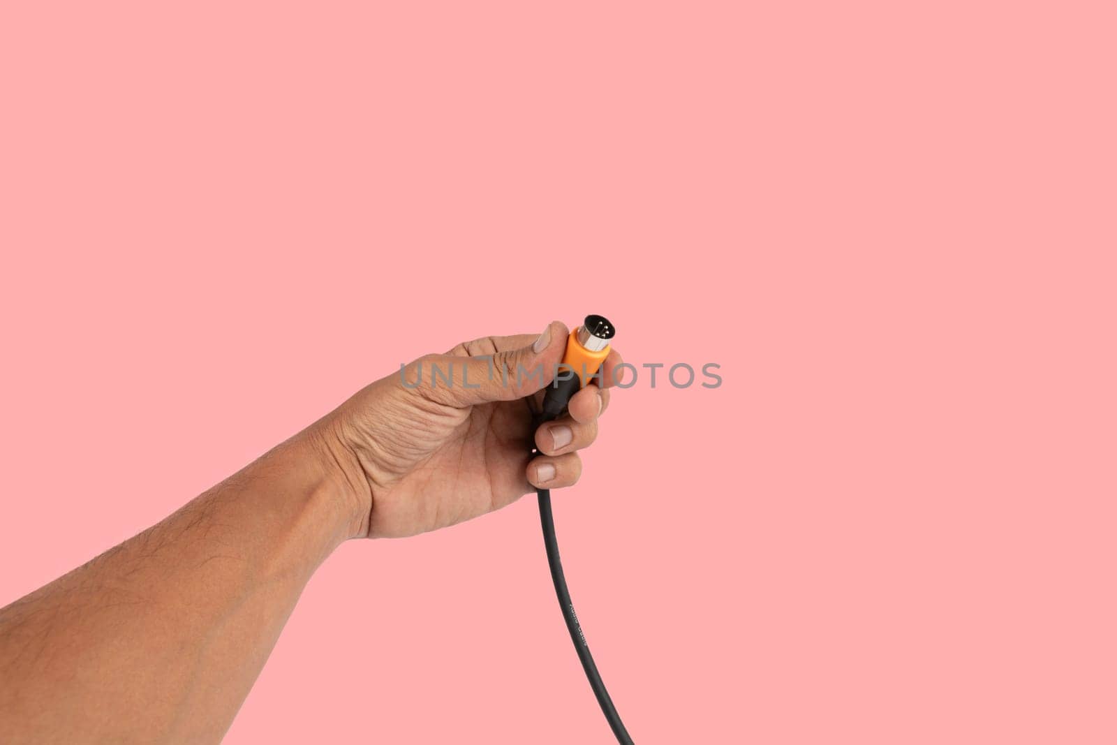Black male hand holding a MIDI audio cable isolated on pink background. High quality photo