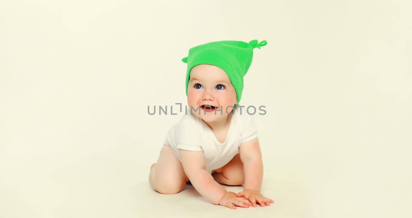Happy baby in green hat playing on the floor on white studio background by Rohappy