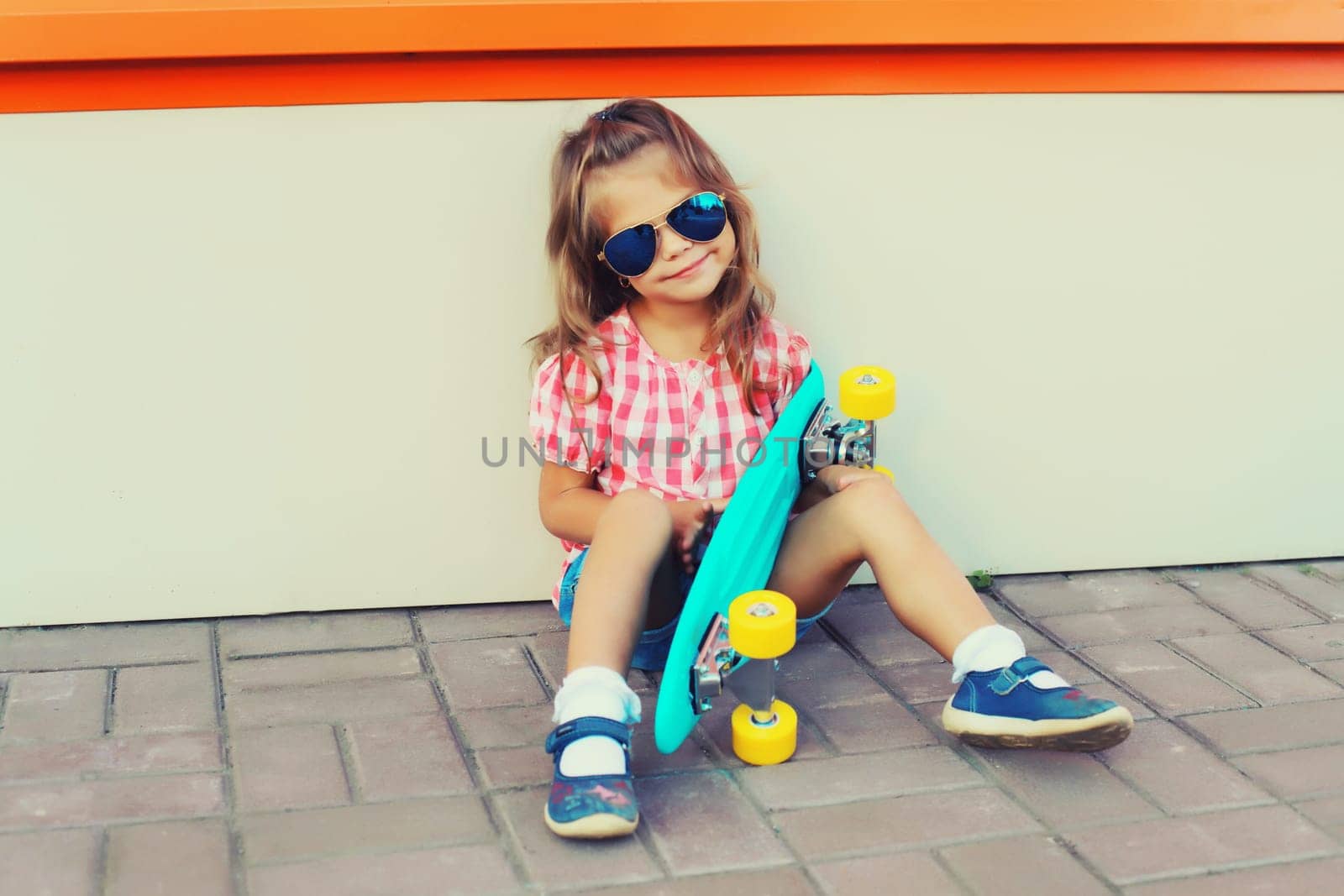 Portrait of stylish little girl child posing with skateboard on city street