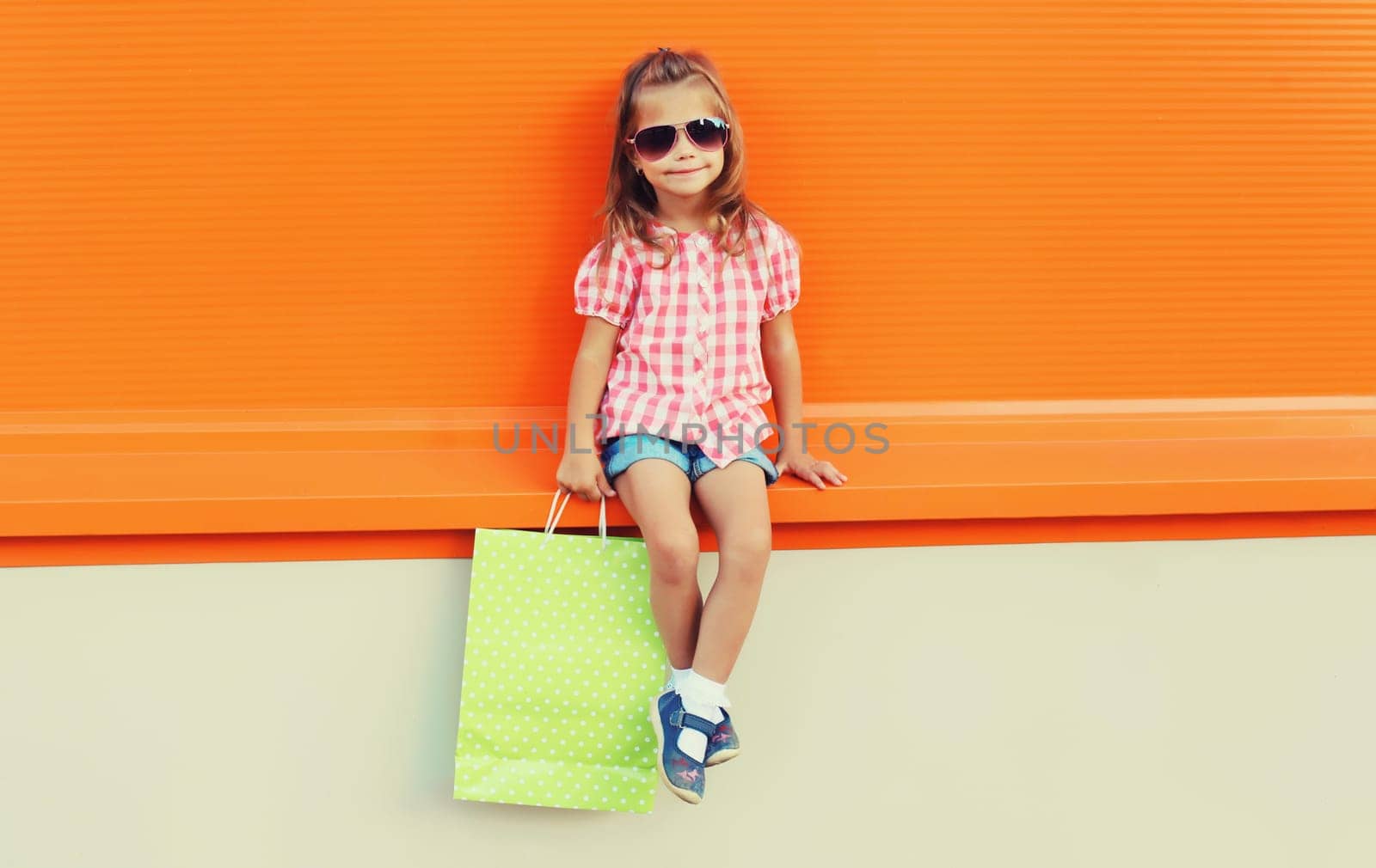 Little girl child with shopping bags posing on city street by Rohappy
