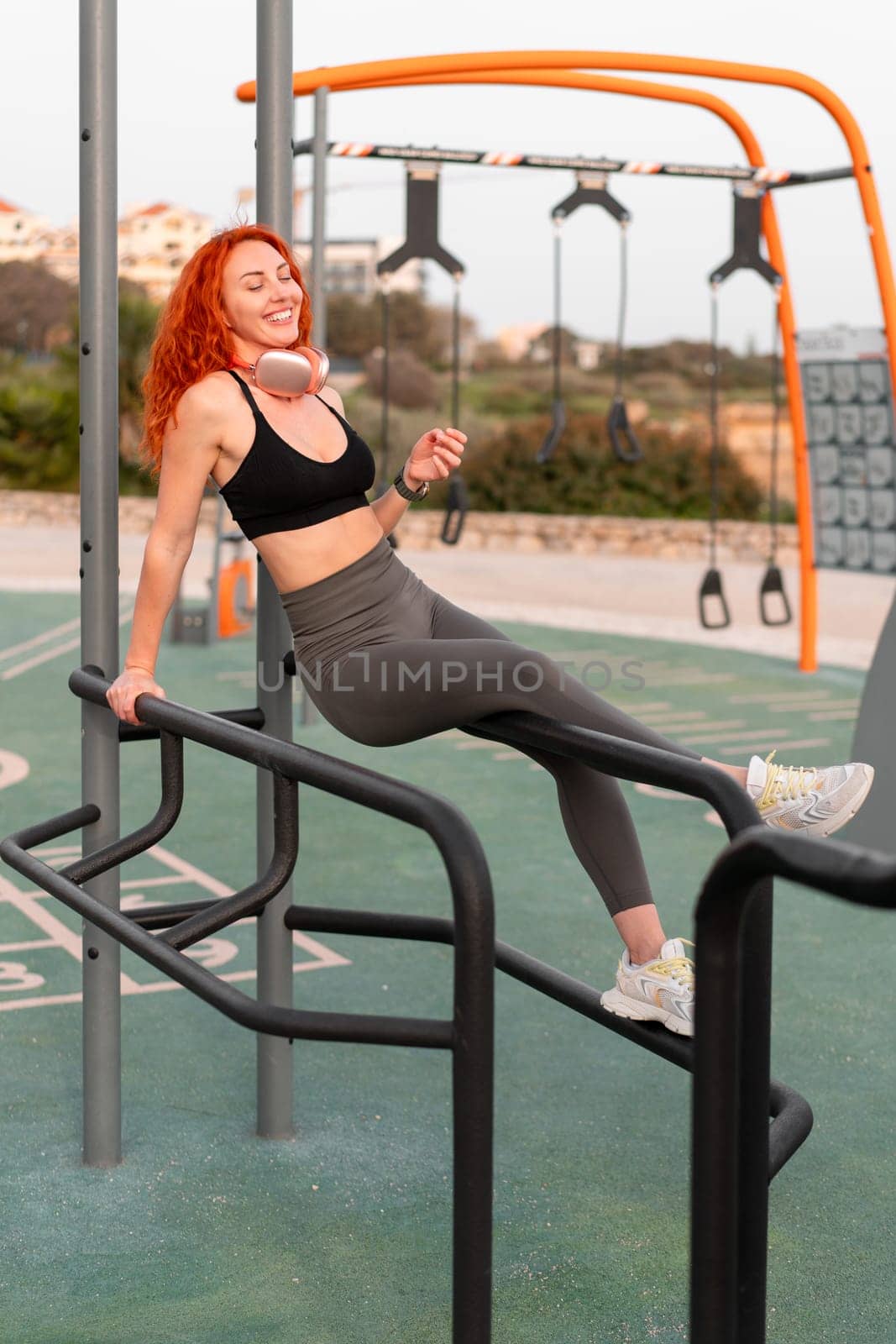 Happy woman jogger sitting on exercise equipment at gym park by andreonegin