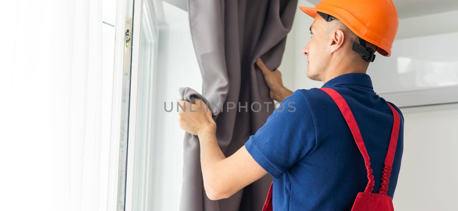 Young man installing curtains over window.