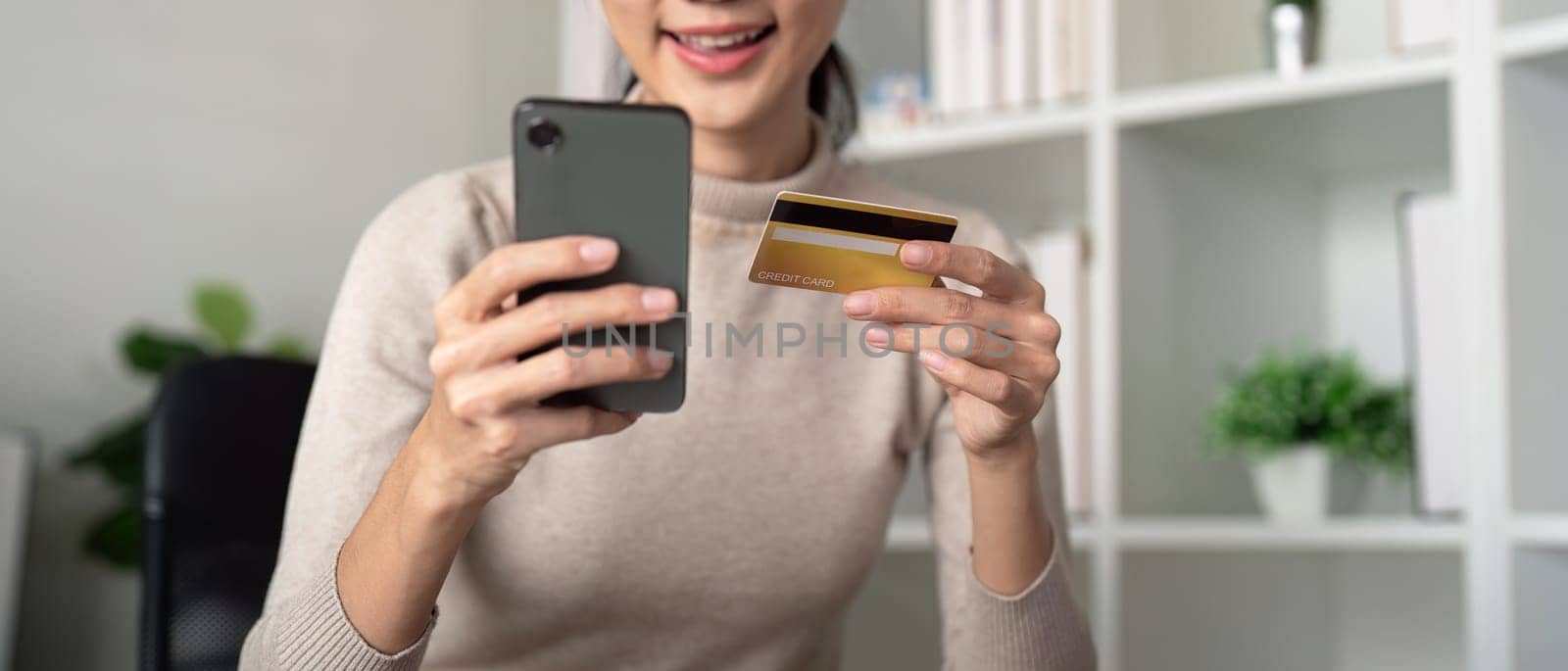 Asian female holding smartphone and credit card, using mobile banking app or online shopping app.