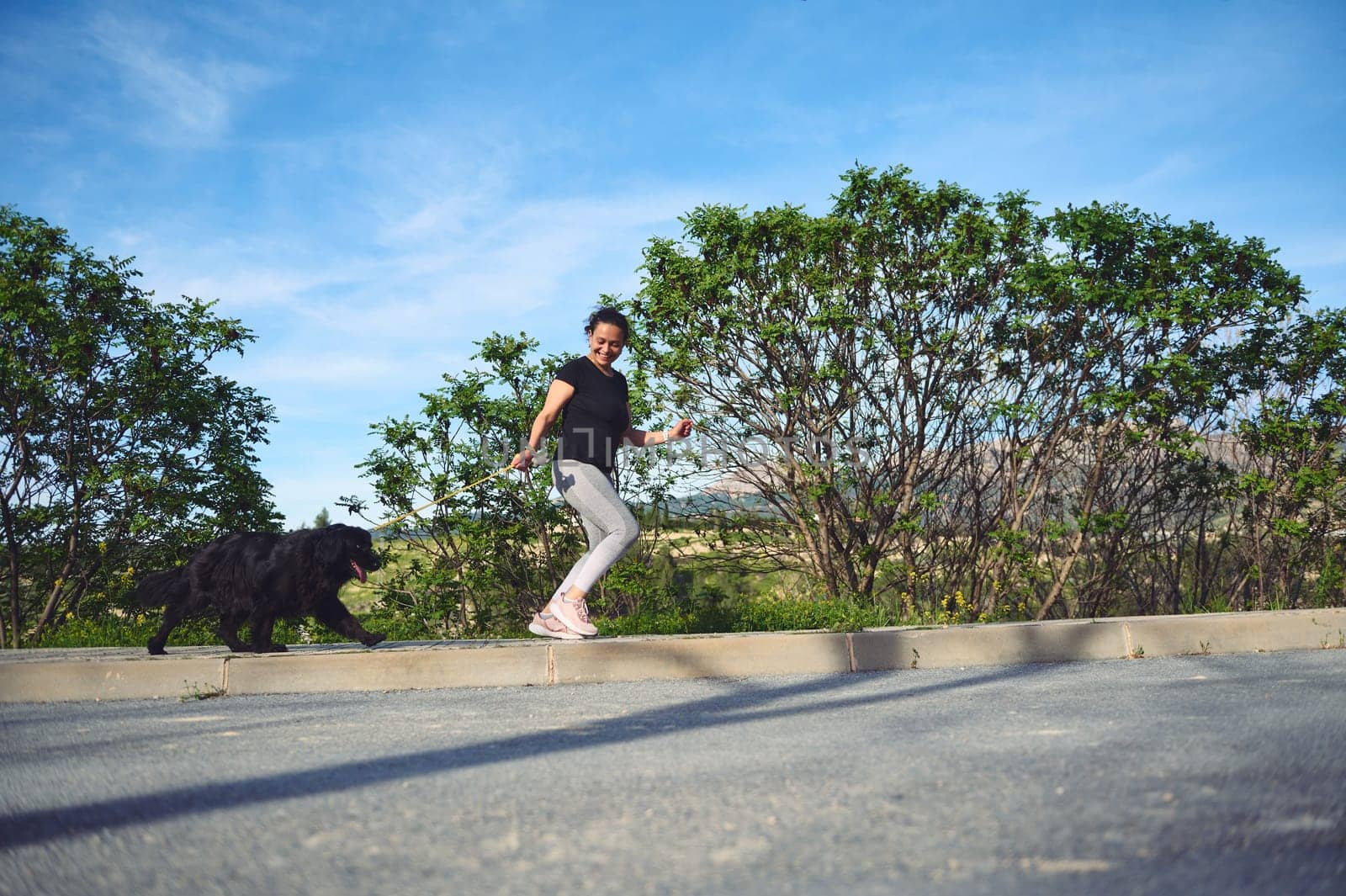 Full length authentic portrait of a young active woman jogging with her dog as a fun way to exercise outdoors. Playing pets concept