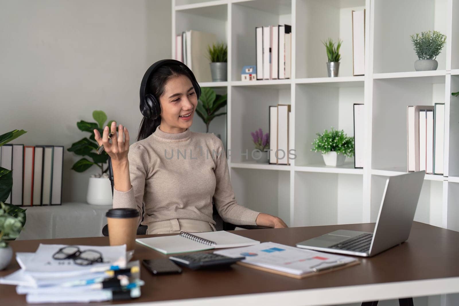 Young businesswoman wearing headphones and discussing project detail with clients on video call. woman with headphones conducting online meeting with colleagues.