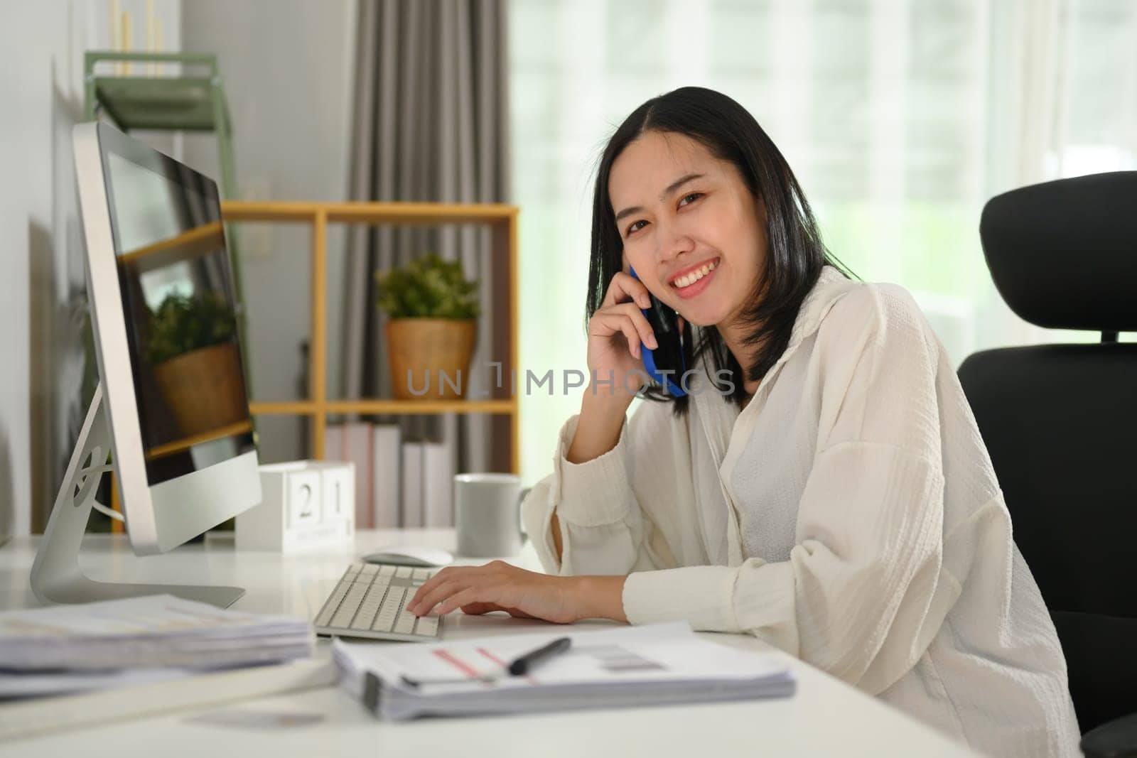 Beautiful businesswoman sitting at working desk and talking on mobile phone.