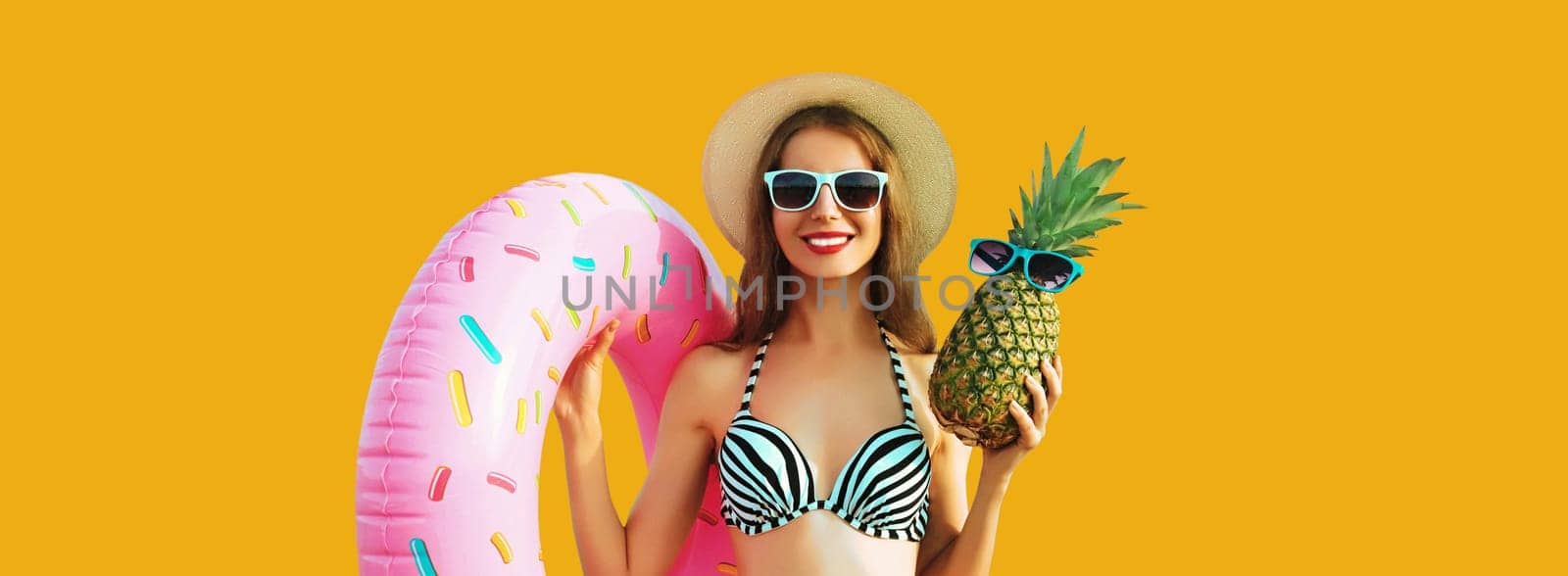 Summer vacation, tourism, happy smiling young woman with swimming inflatable ring and pineapple wearing straw hat on yellow studio background