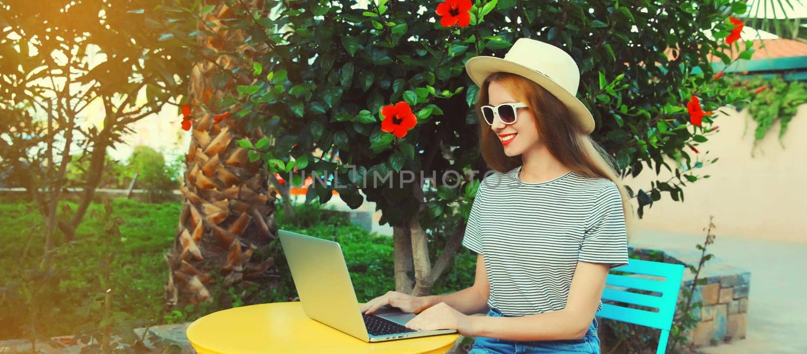 Happy young woman working with laptop sitting at the table in street cafe in summer park