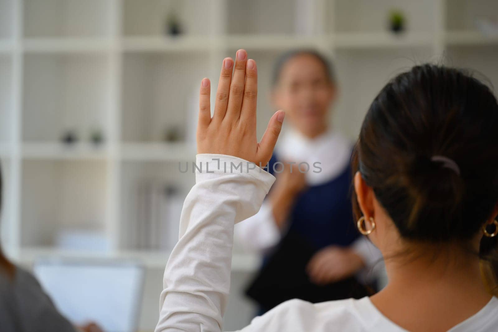 Back view of female college student raising hand to answering a question during lecture.