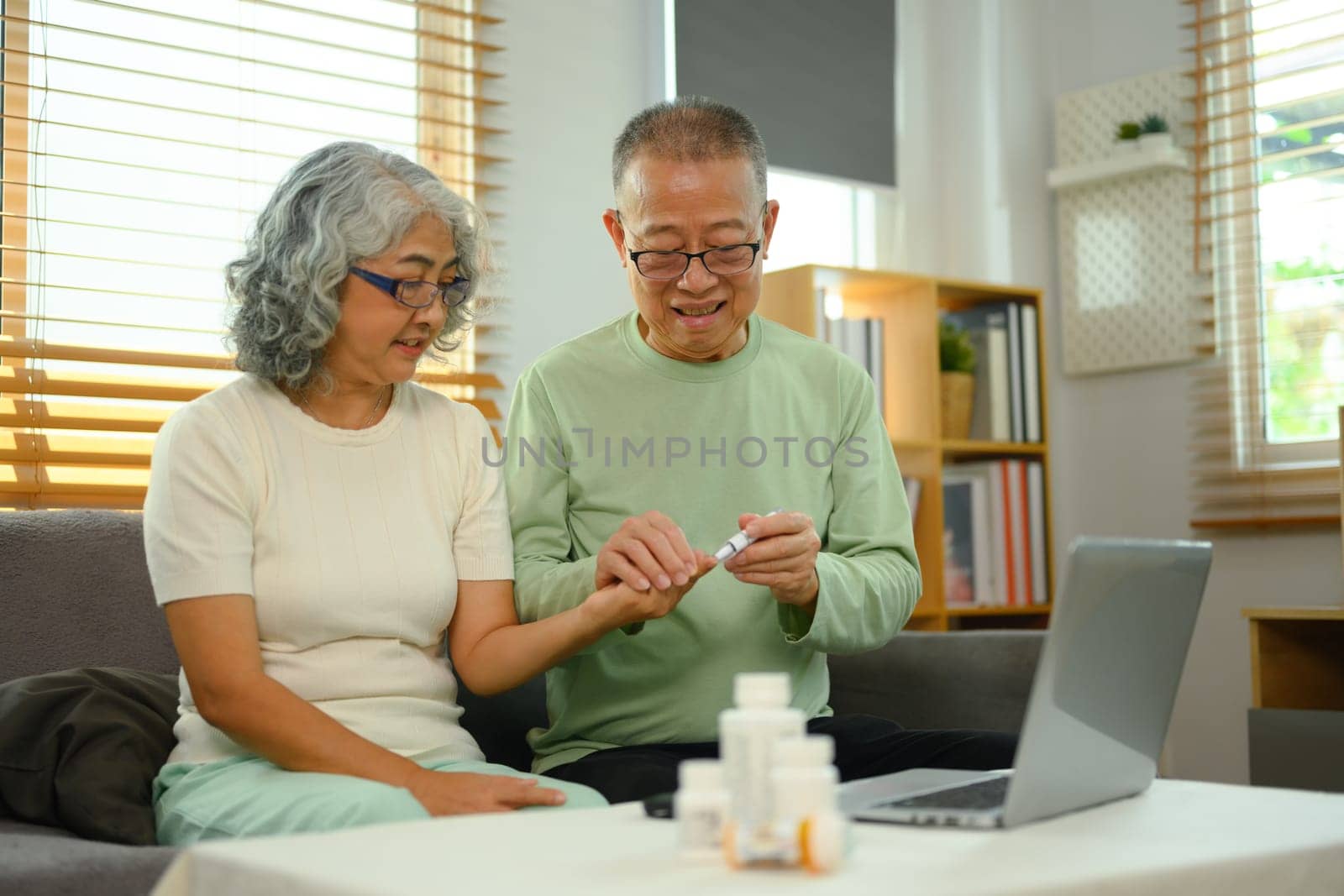 Senior husband helping his wife checking blood sugar level with glucometer at home. Health care concept by prathanchorruangsak