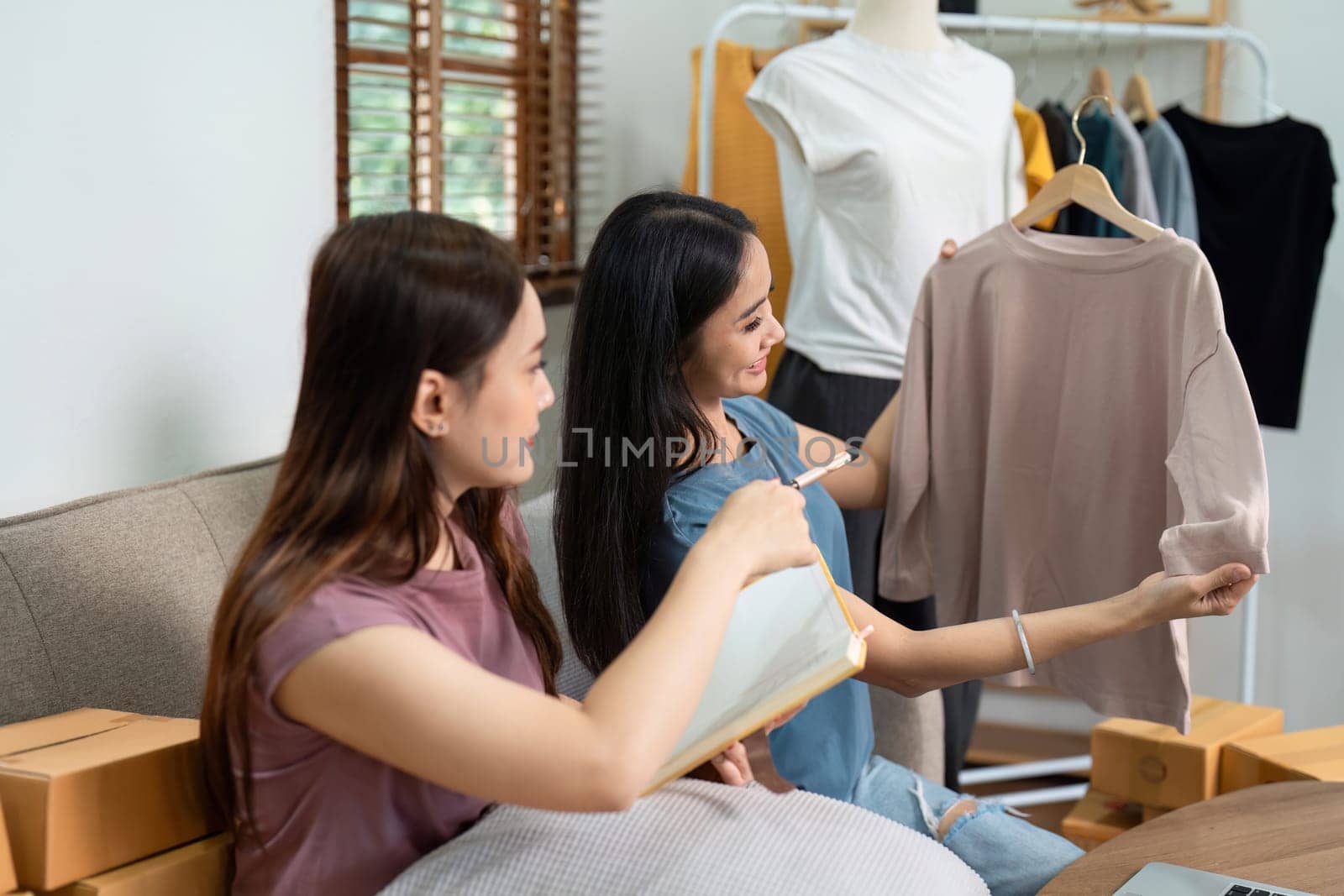 Asian woman friends couple talk to camera to sell the clothes at home. Young attractive business people female live streaming and showing clothing to customer in online by itchaznong