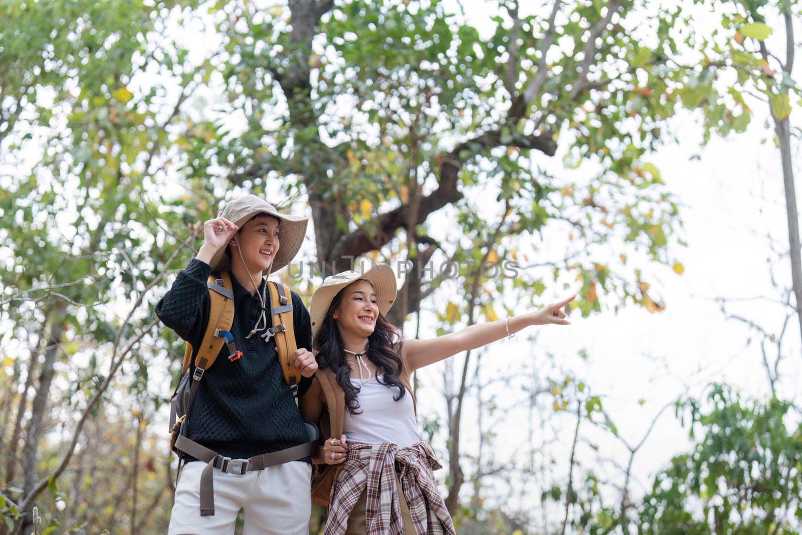 Cheerful romantic lesbian couple traveler with backpack on their backs go hiking through the forest in the mountains in summer by nateemee