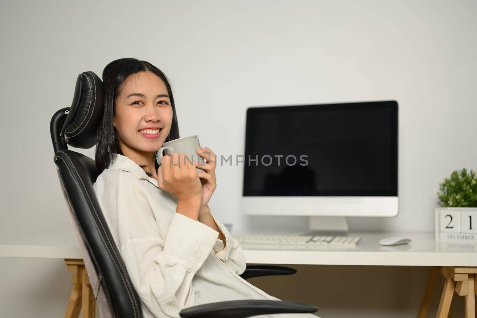Attractive young businesswoman drinking coffee at the desk in the office.