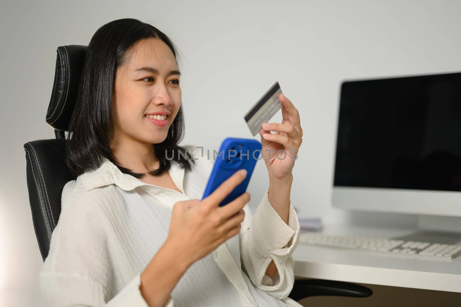 Pleased young woman with credit card in hands making internet order purchase on mobile phone.