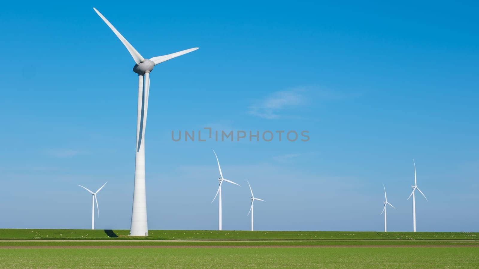 A group of wind turbines dance gracefully in a lush green field under the clear blue sky, harnessing the power of the wind to generate clean energy.
