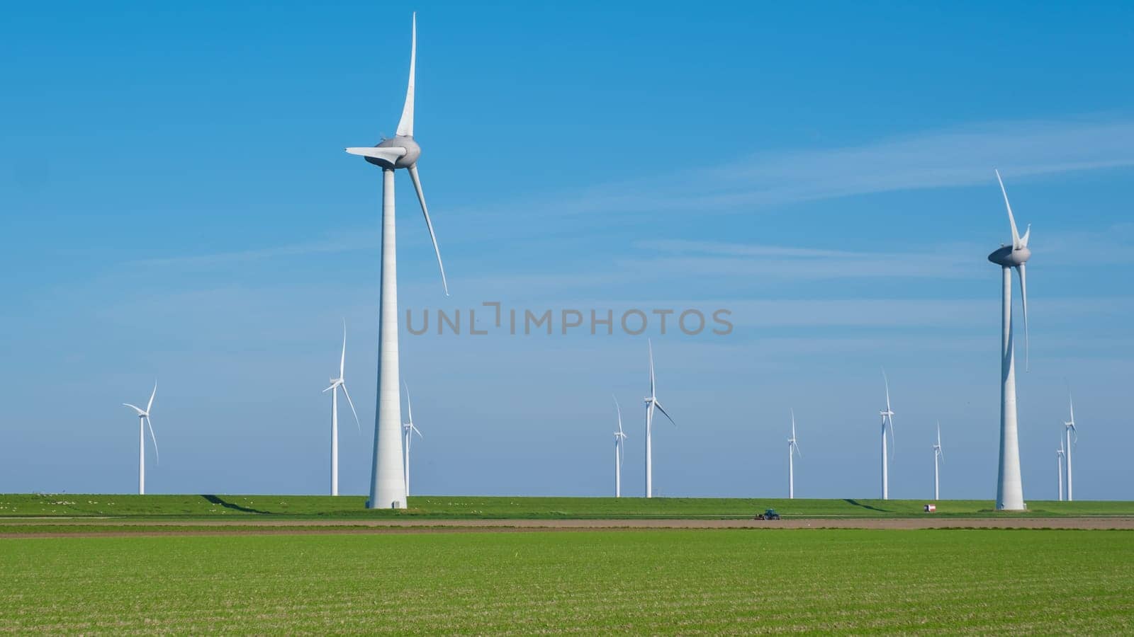 A serene field of vibrant green grass stretches out before us, dotted with a collection of majestic windmills spinning gracefully in the background.